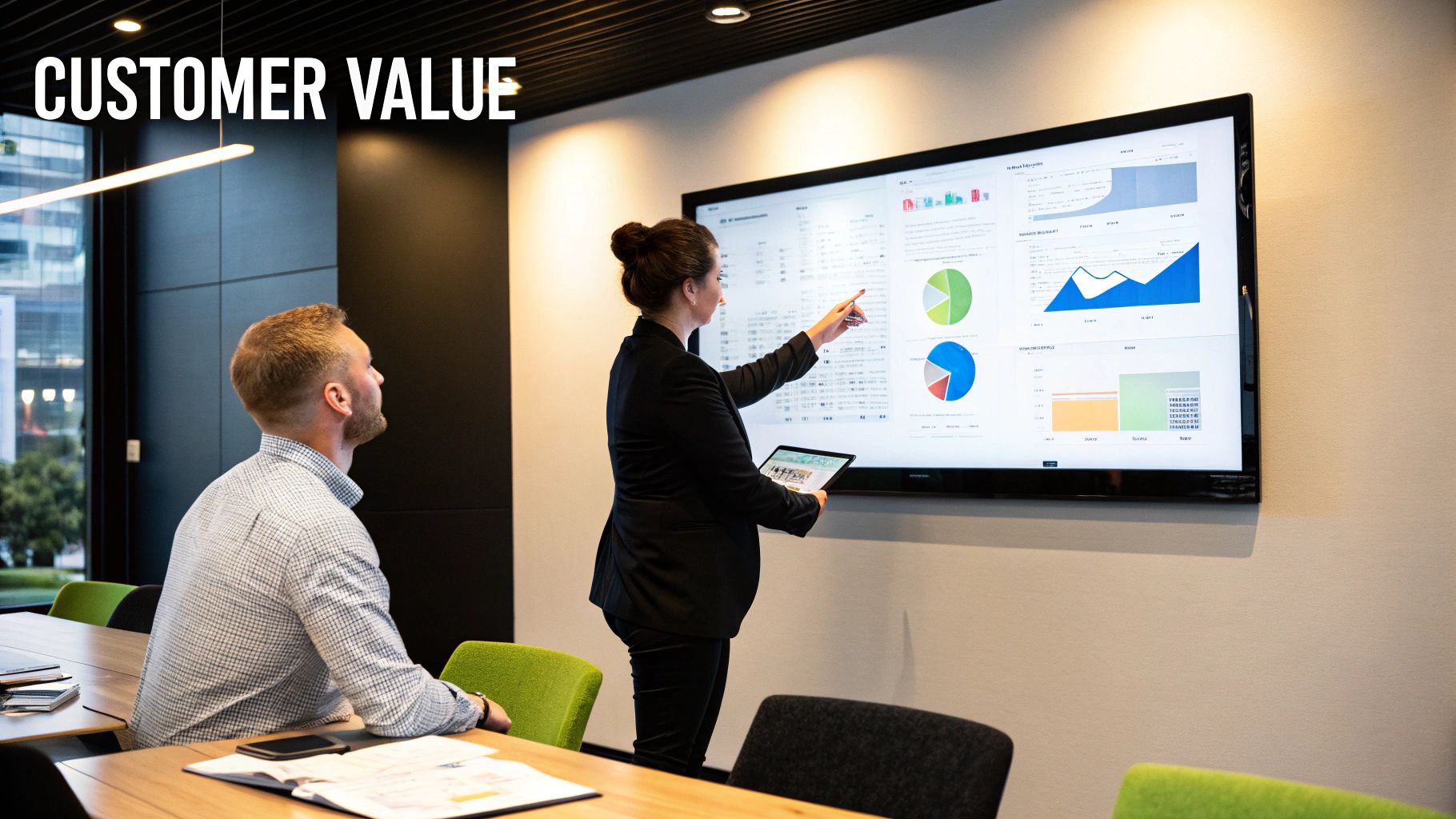 Business meeting showcasing customer value metrics, woman presenting data on screen with charts and graphs, man observing, modern office setting.